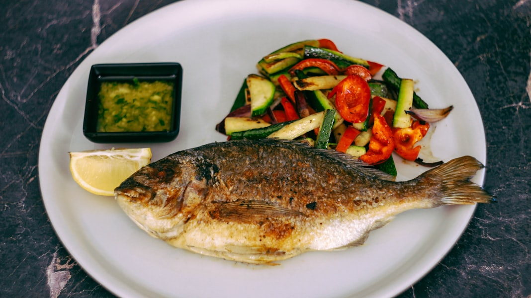 a white plate topped with a fish next to a salad