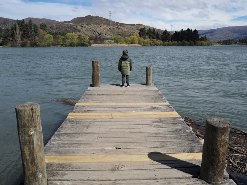 Child standing on a wooden dock by the lake.