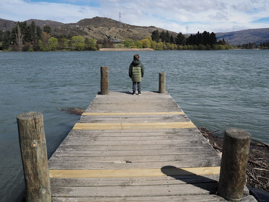 Child standing on a wooden dock by the lake.