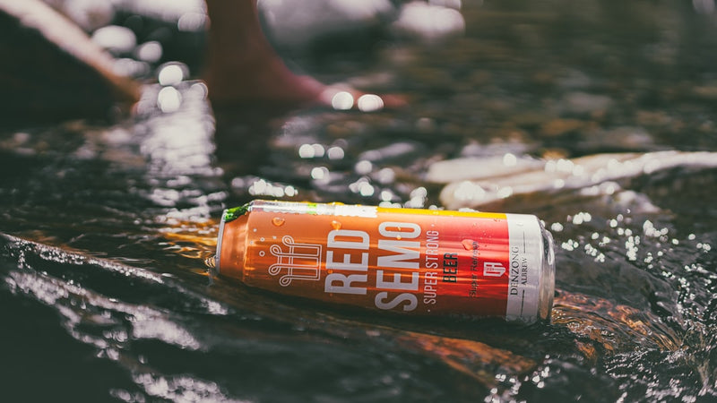 A can of red semo beer floats in a stream.