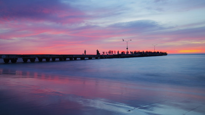 Pier at sunset with colorful sky and calm ocean.