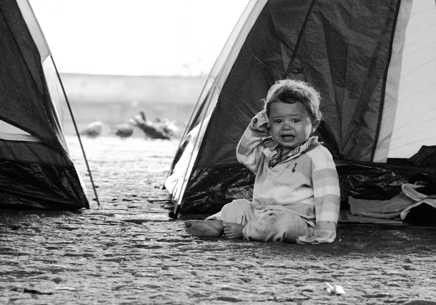 A crying baby sits between two tents.