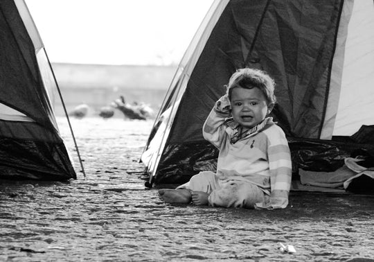 A crying baby sits between two tents.